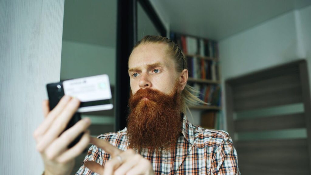 Hombre con el móvil y una tarjeta en la mano: por qué no hay cajeros de Bitcoin sin KYC en España