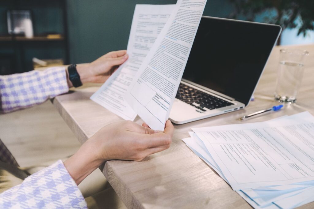 Manos revisando papeles impresos junto a un portátil, como al contrastar el aviso legal de una web con el registro de la CNMV
