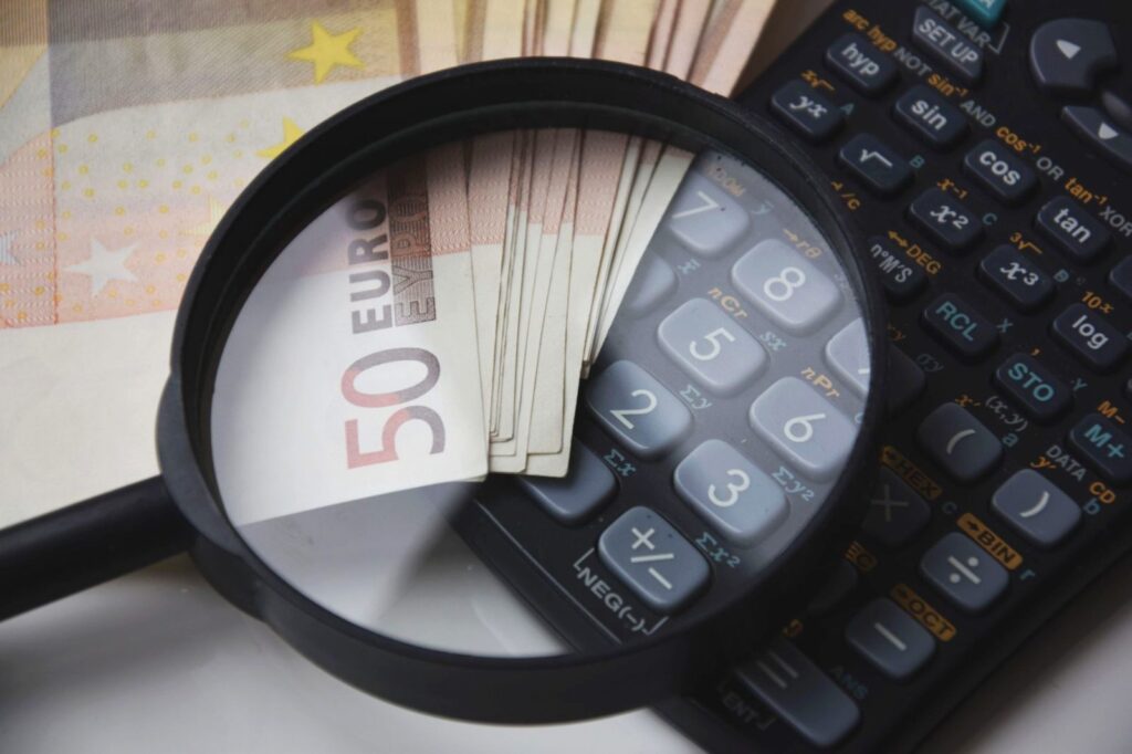 Billetes de 50 euros bajo una lupa junto a una calculadora: cómo se calcula el límite de efectivo