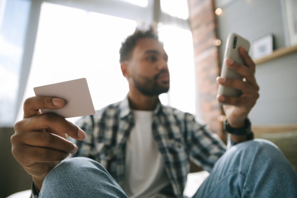 Hombre con el móvil y una tarjeta en la mano verificando su identidad para una transferencia de criptomonedas