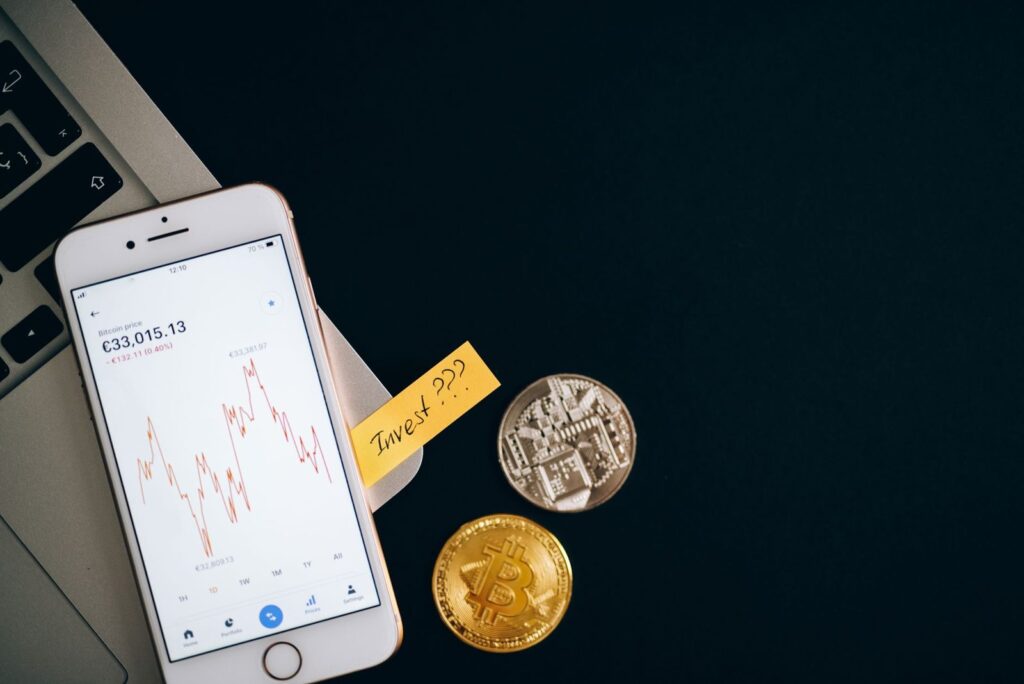 Móvil con precios de criptomonedas junto a monedas y un portátil: comprar stablecoins en España