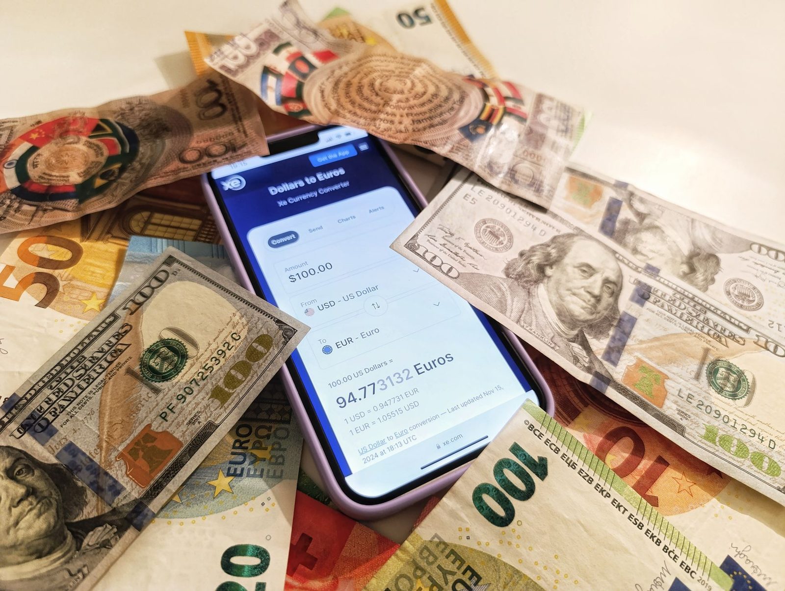 Móvil con un conversor de dólares a euros sobre billetes: las stablecoins replican el valor de una moneda