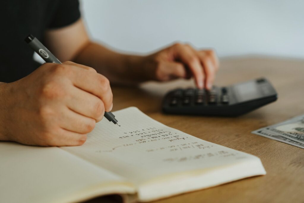Persona haciendo cuentas en un cuaderno con una calculadora al lado