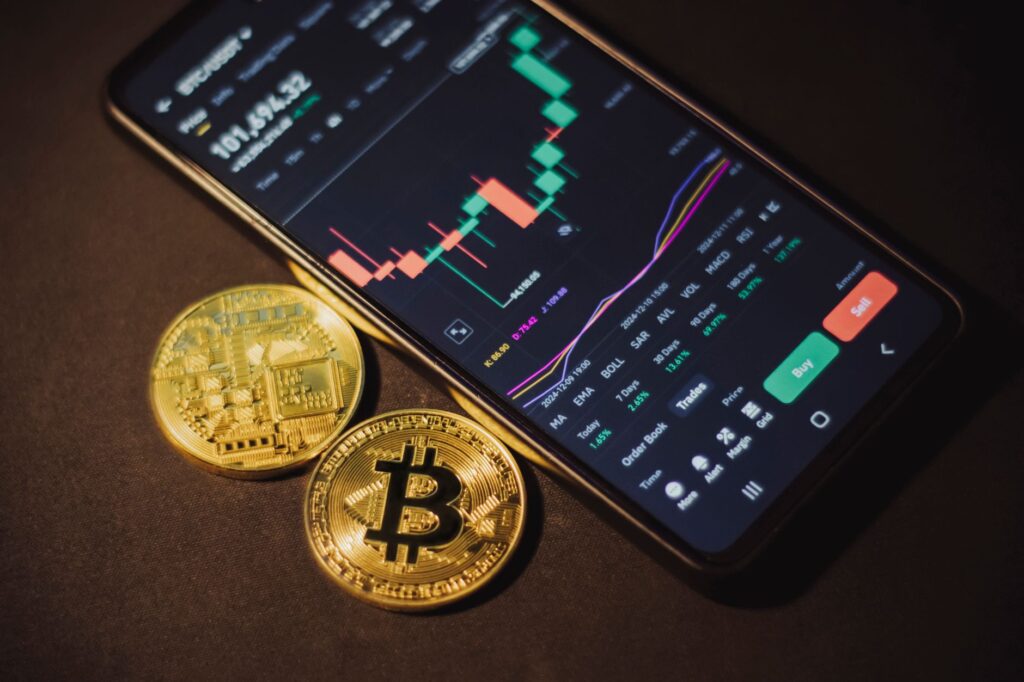 Móvil con una app de criptomonedas junto a dos monedas de bitcoin sobre una mesa oscura